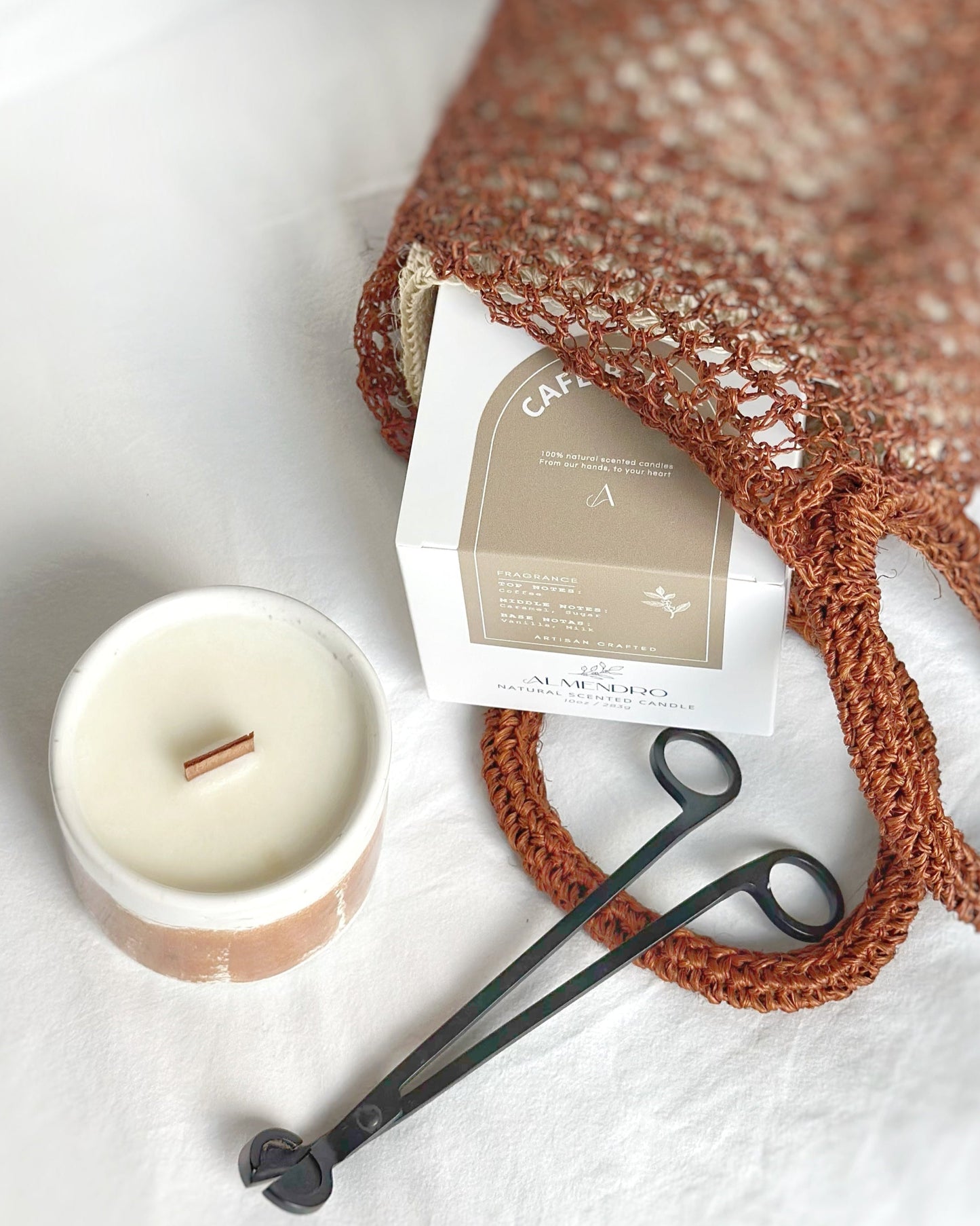 Brown woven bag with a product inside, next to a candle and black scissors on a white surface.