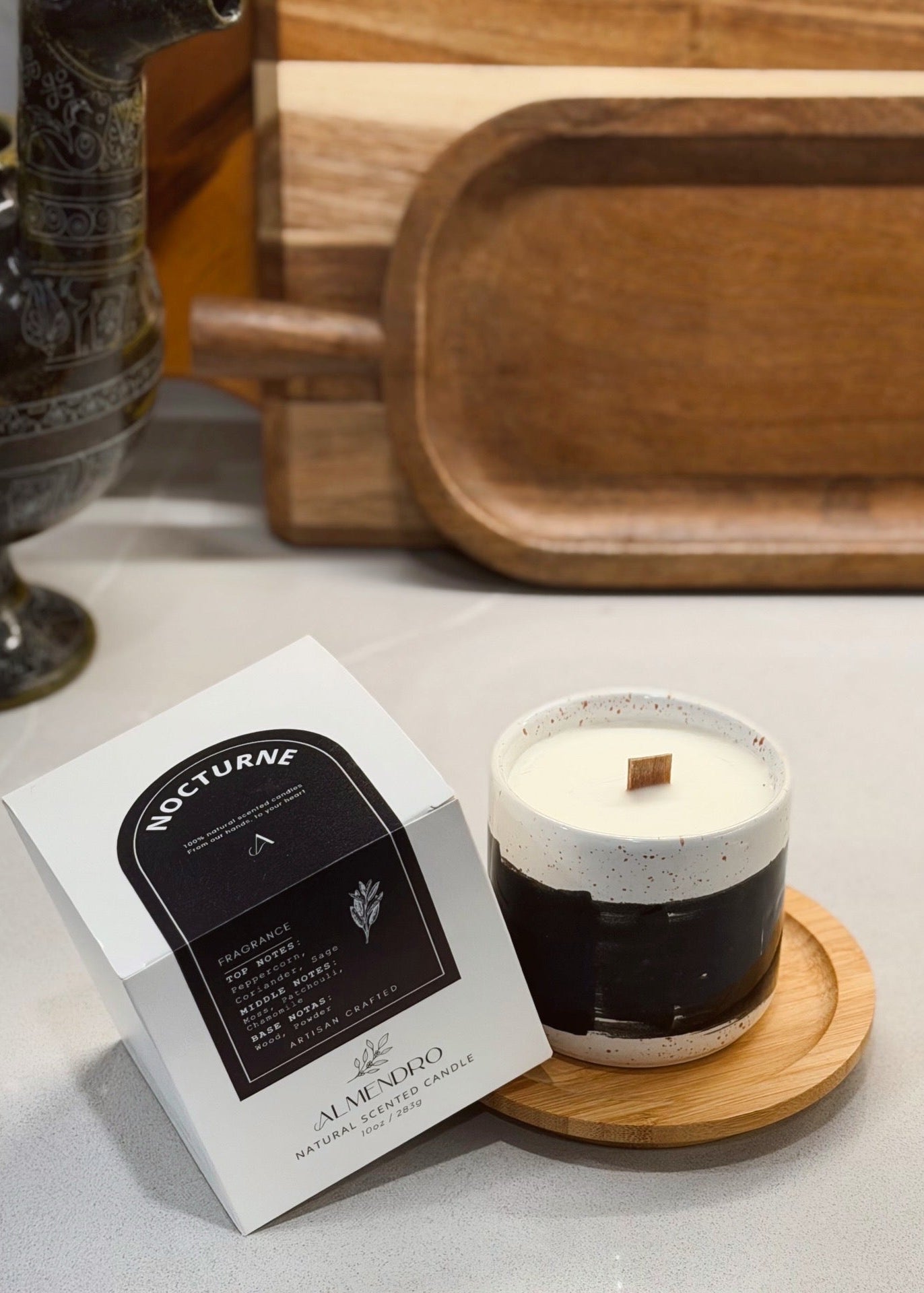 Candle with packaging on a surface with a wooden tray in the background