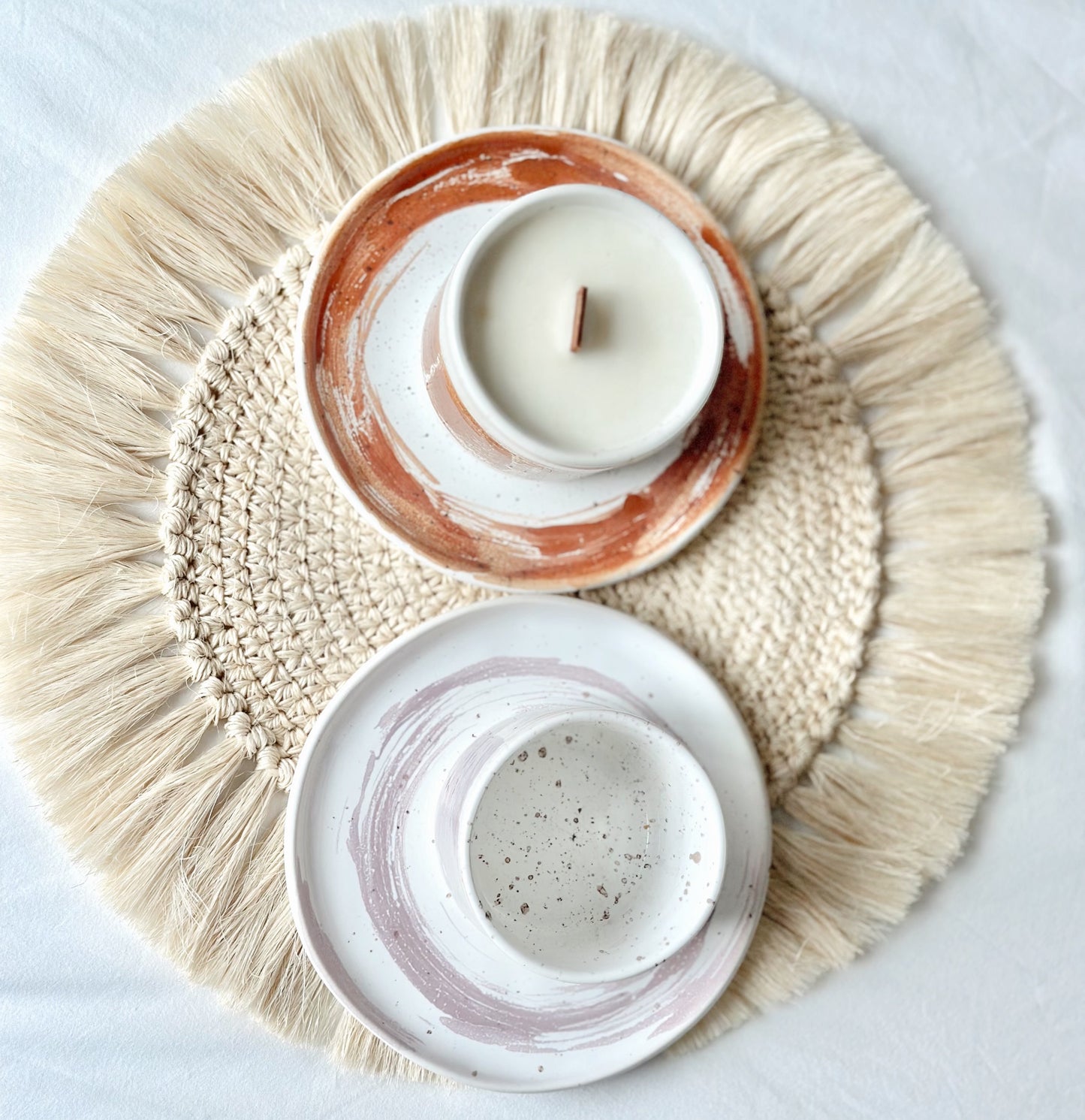 Two ceramic candle holders on a textured woven mat with a white background